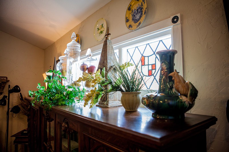A beautifully decorated interior space with a variety of plants and vases on a wooden table beneath stained glass windows.