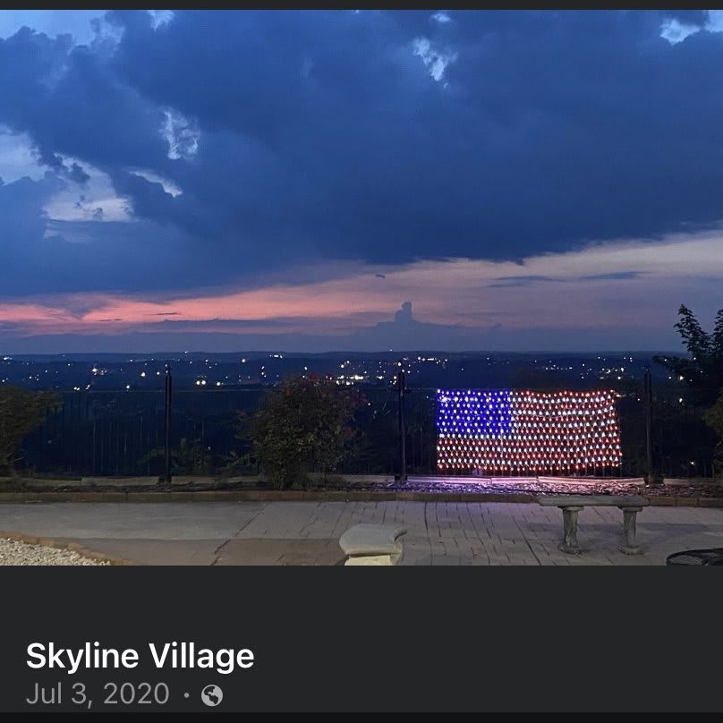 A scenic sunset view over Skyline Village with an illuminated American flag display.