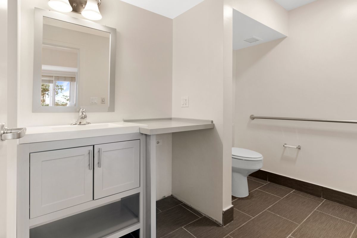 A modern bathroom with a sink, mirror, and toilet, featuring a countertop space and tiled flooring.