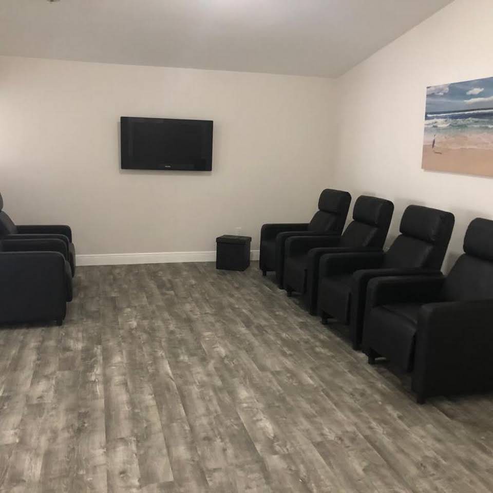 A minimalist home theater setup with multiple recliner chairs, a wall-mounted television, and modern wood flooring.