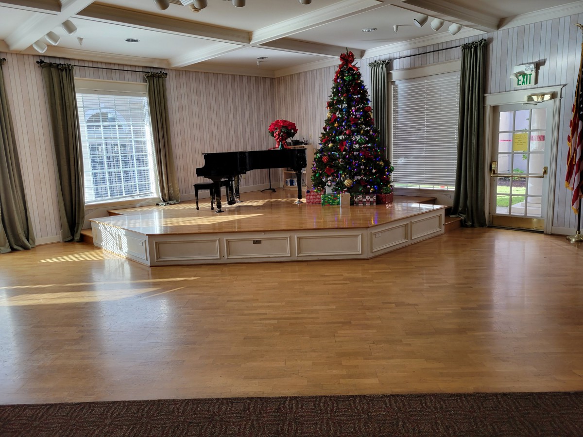 A decorated stage featuring a piano and a Christmas tree with gifts in an indoor setting.