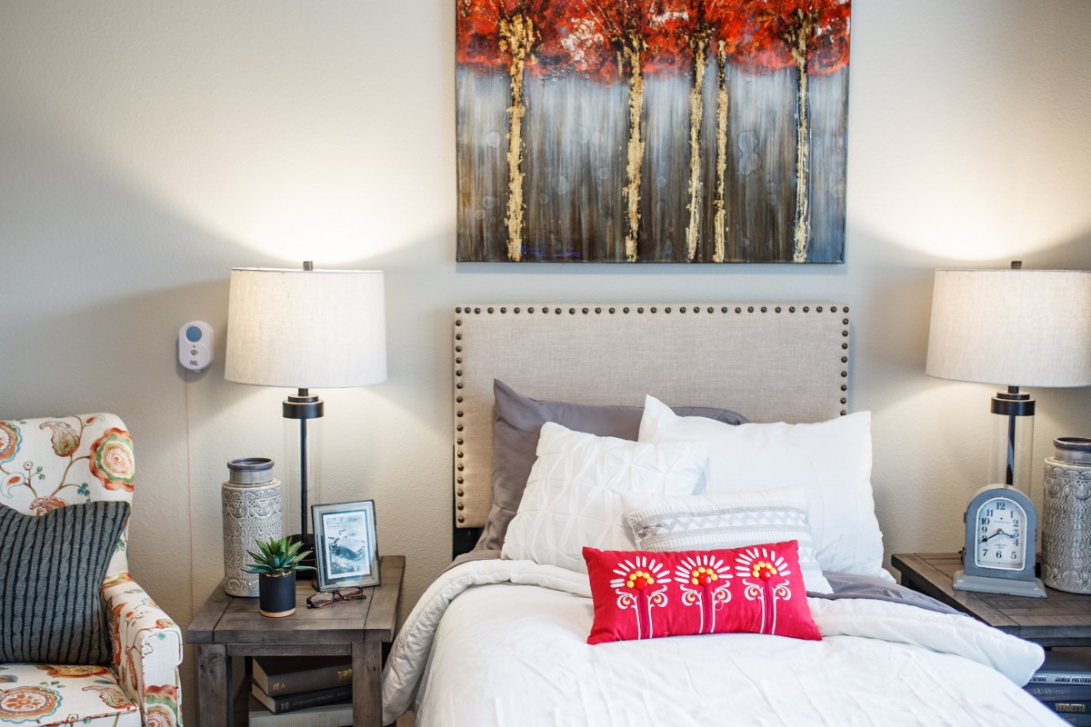 A cozy bedroom with a decorative painting and colorful cushion on the bed.