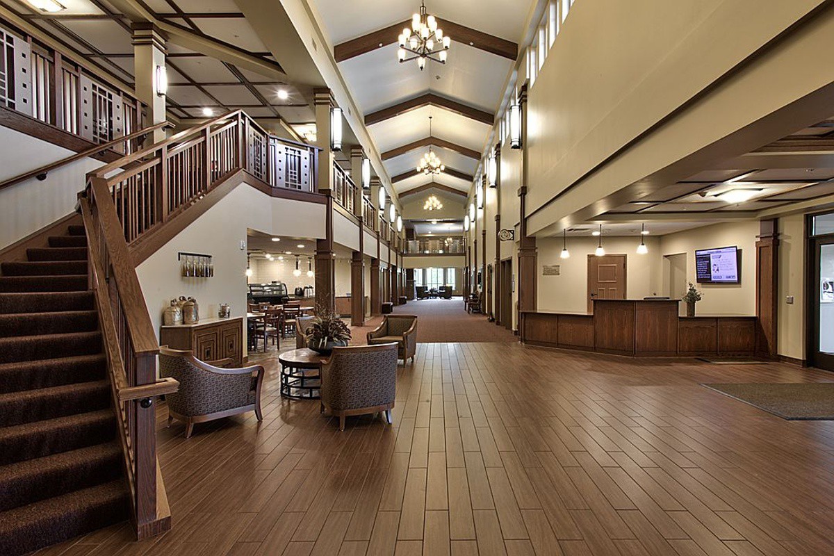 A spacious hotel lobby with elegant wood flooring, cozy seating areas, and a high ceiling adorned with chandeliers.