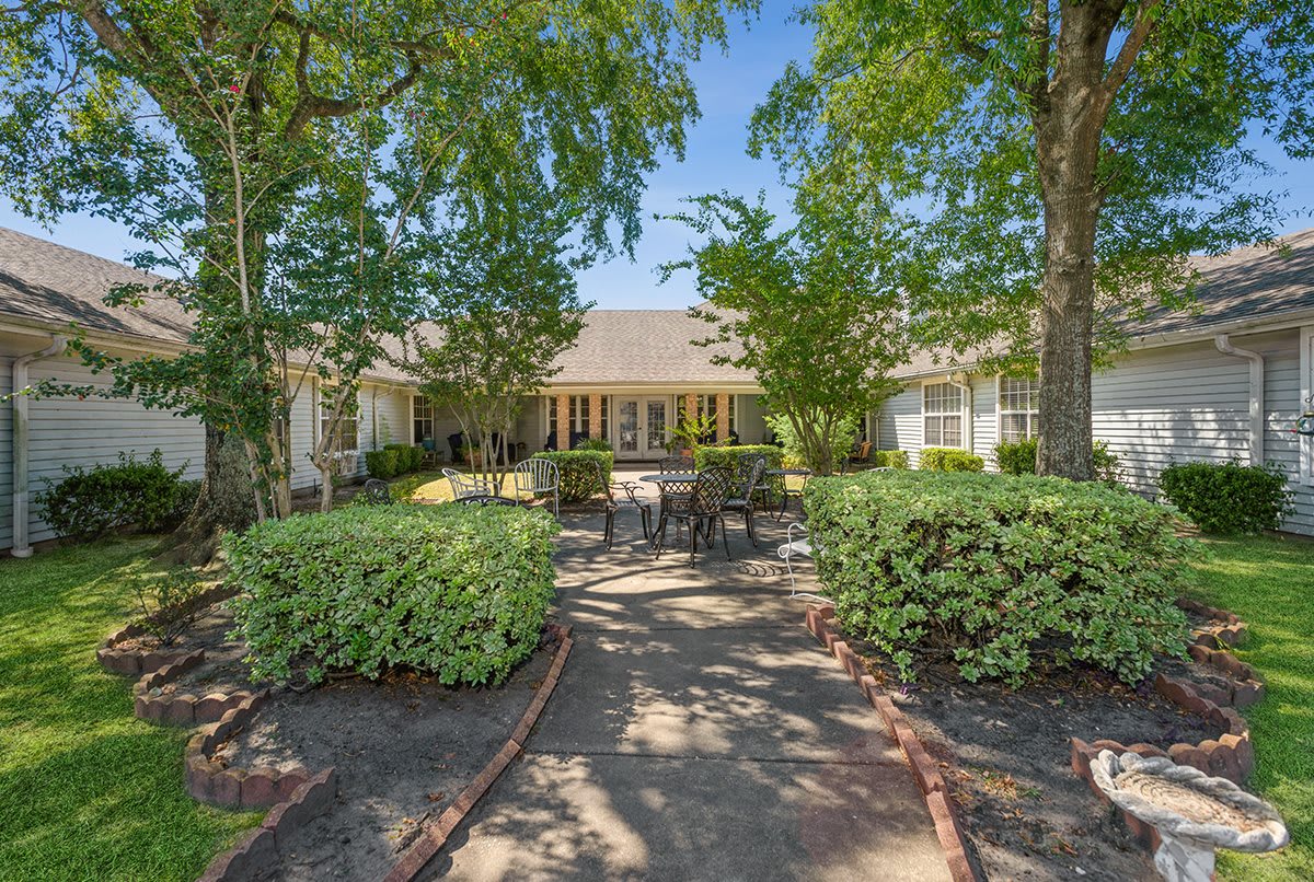 A serene garden setting with a patio and outdoor furniture, surrounded by lush greenery.