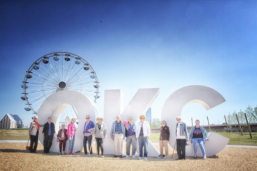 A cheerful group of visitors posing in front of the iconic 'OKC' sign with a ferris wheel in the background.