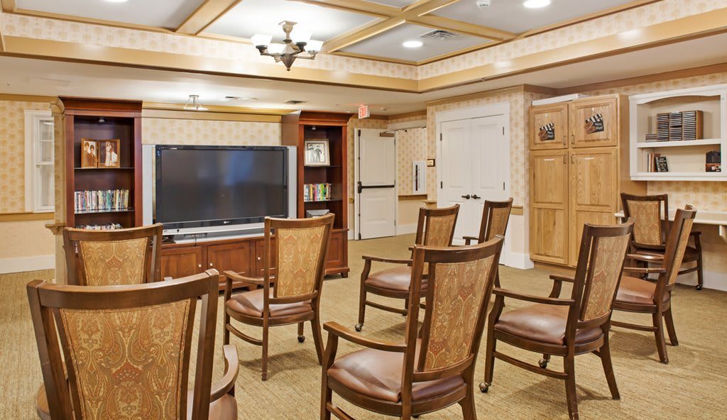 A comfortable conference room with wooden chairs arranged around a large television.