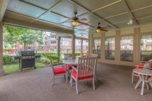 A cozy covered patio with a dining setup, ceiling fans, and a garden view.
