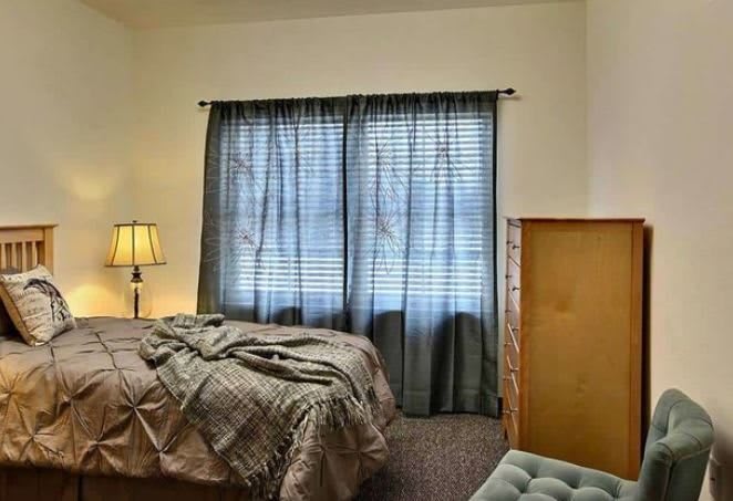 A cozy bedroom with a bed, lamp, and window curtains.