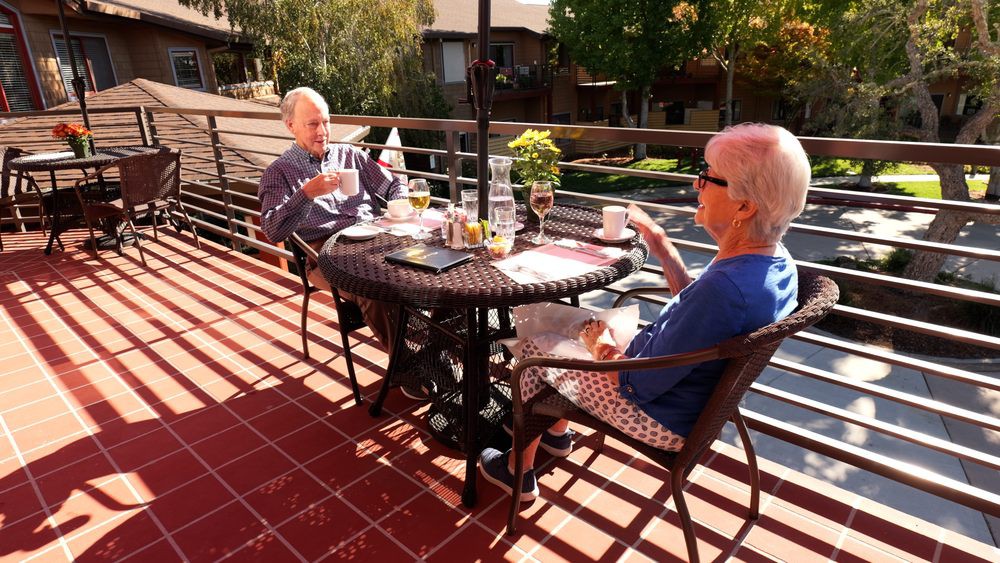 A couple enjoys a relaxing conversation over coffee on a sunny patio.