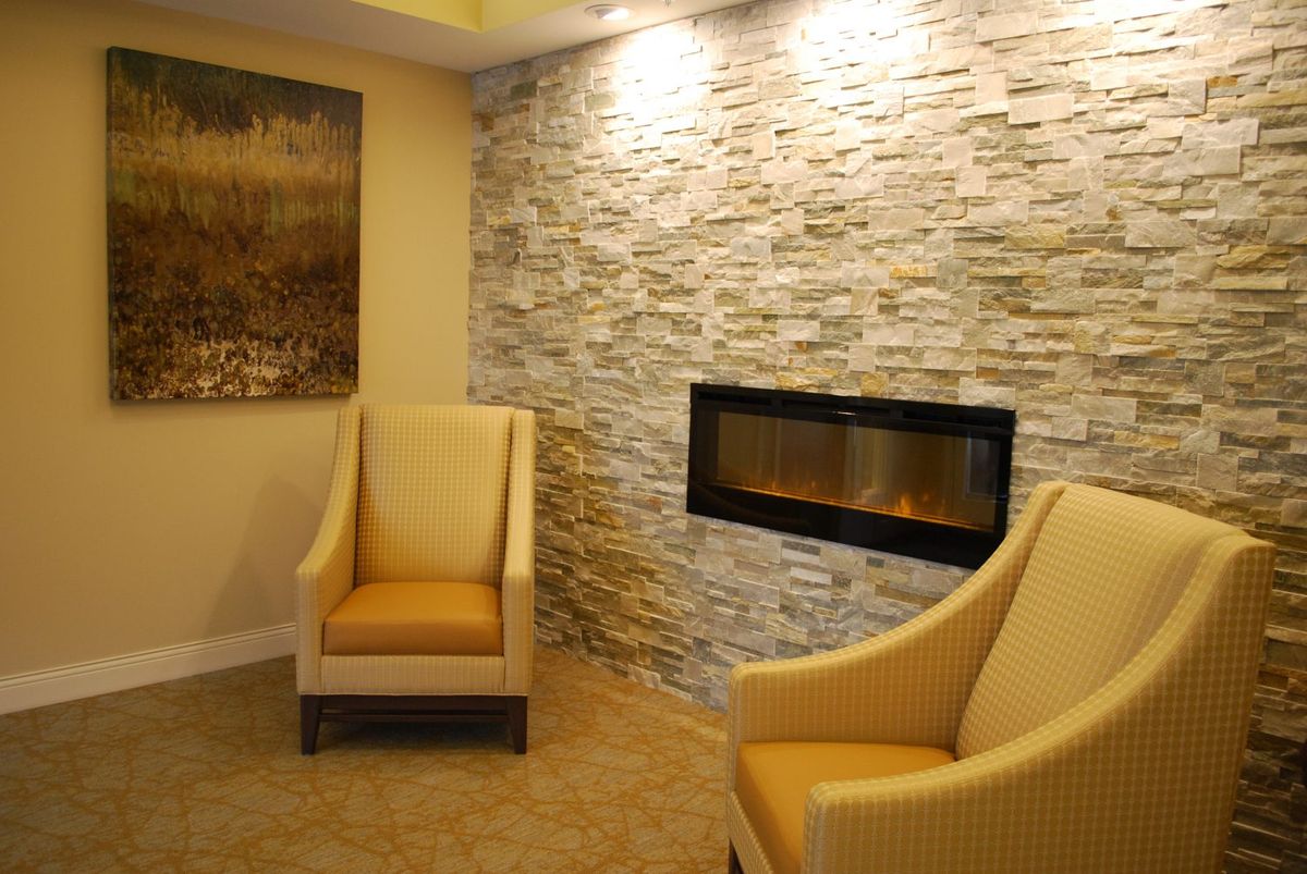 A modern living room featuring a stone wall with a built-in fireplace, paired with comfortable armchairs.