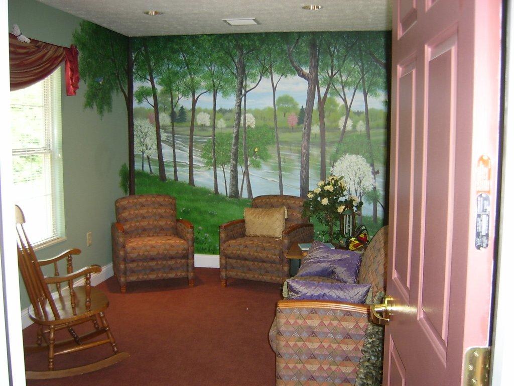 A cozy room featuring a forest mural, comfortable chairs, and decorative plants.