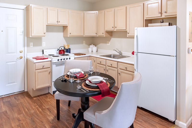A cozy kitchen with a small dining area, featuring light-colored cabinets, a white refrigerator, and a set table for two.