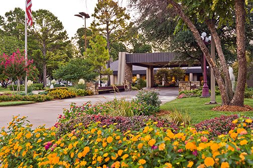 A beautifully landscaped area with vibrant flowers and lush trees surrounding a building entrance.
