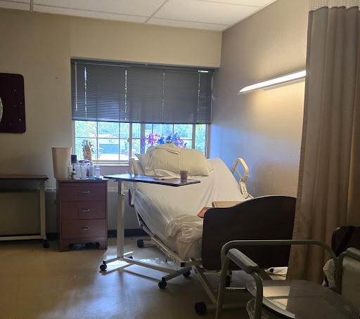 A view of a patient room in a hospital, featuring a bed and natural light coming through the window.