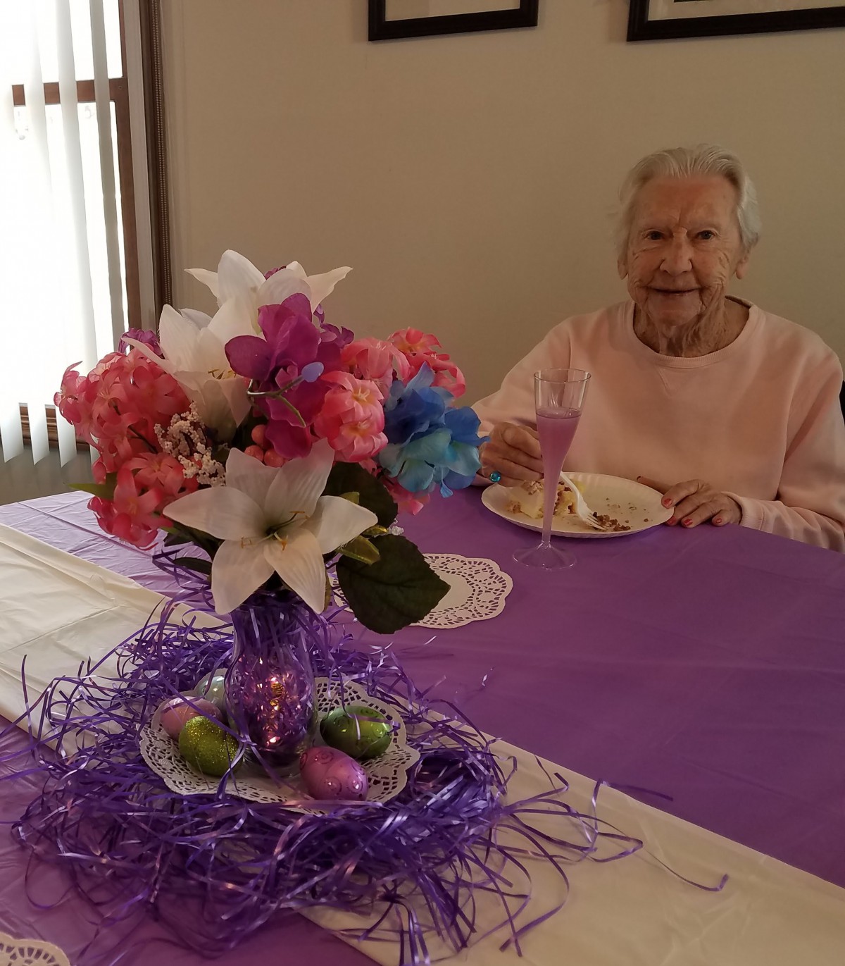 An elderly woman sitting at a decorated table with a floral centerpiece.