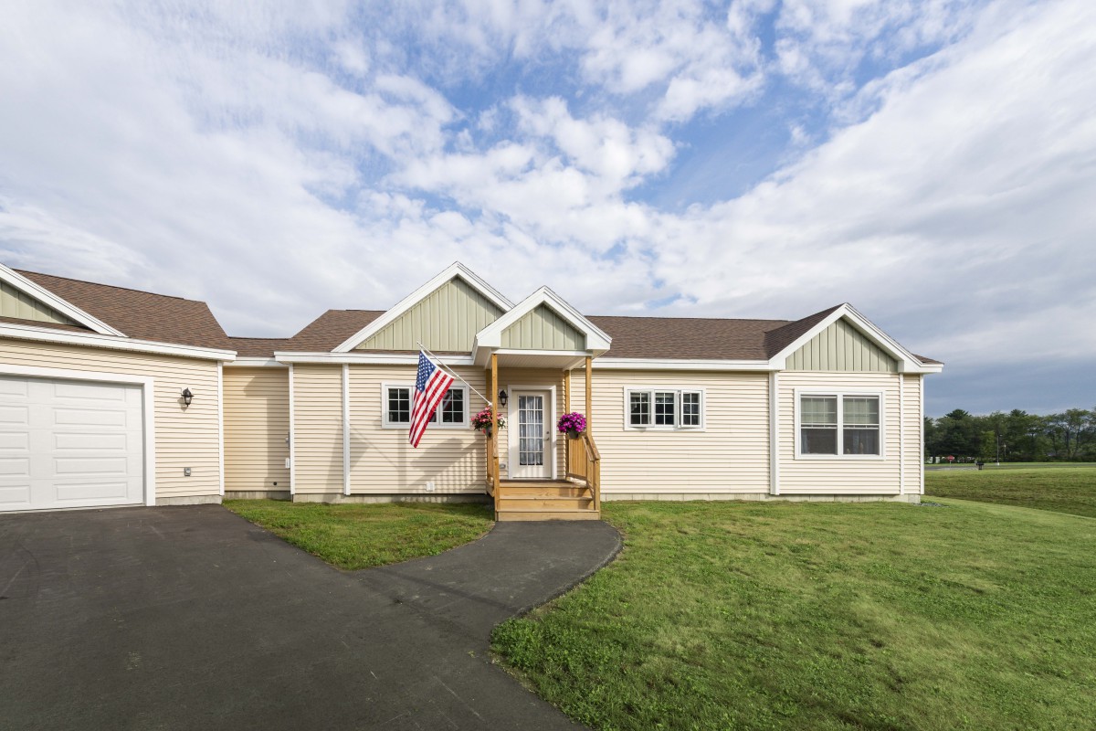 A charming single-story house with a front lawn and driveway, adorned with a flag.