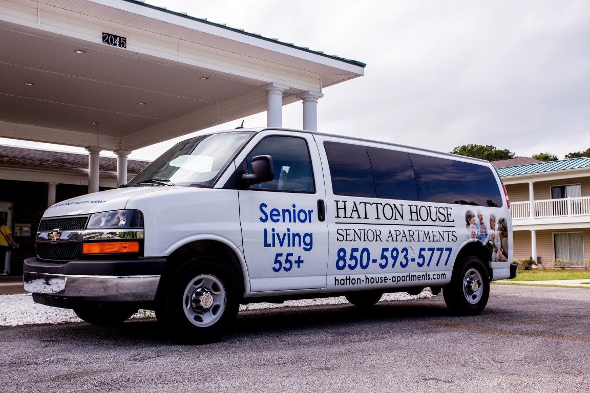 A van parked in front of a building, advertising Hatton House Senior Living for ages 55+.
