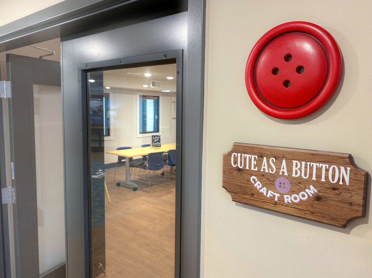 Entrance to a craft room decorated with a large red button and wooden sign.