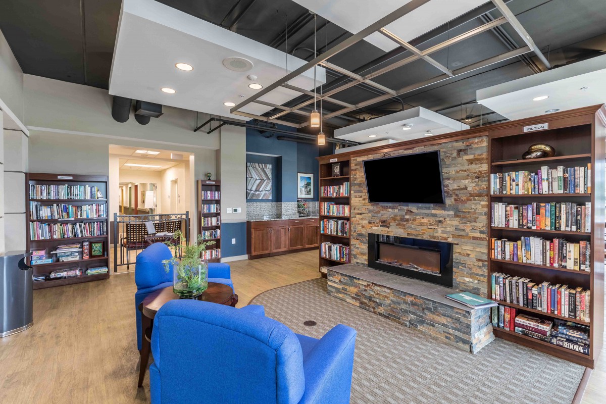 A modern living room with a stone fireplace, mounted TV, and blue chairs for a cozy seating area.