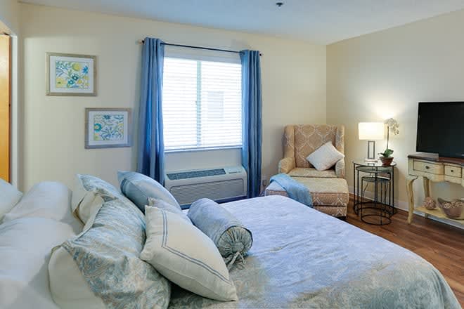 A cozy bedroom with a neatly made bed, a comfortable chair, and soft lighting.