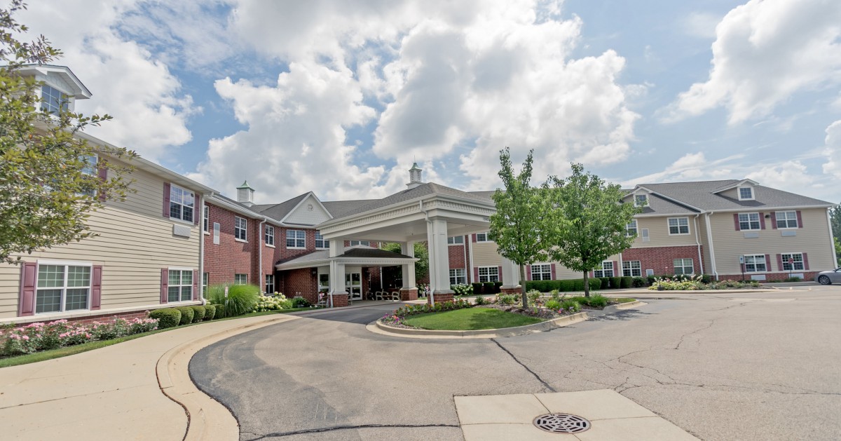 A welcoming building entrance with a curved driveway under a partly cloudy sky.
