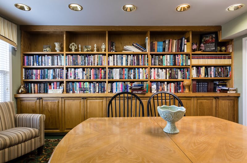 A cozy library with wooden bookshelves filled with books and a dining table in the foreground.