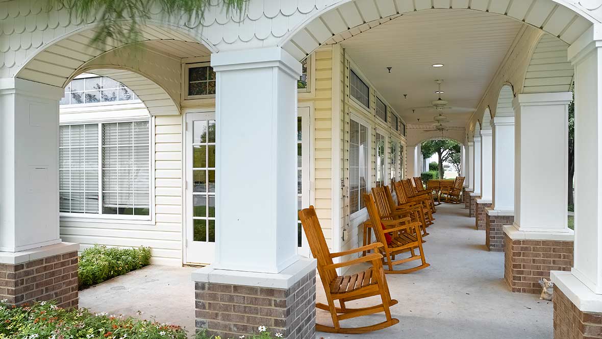 A peaceful porch lined with wooden rocking chairs and decorated columns.