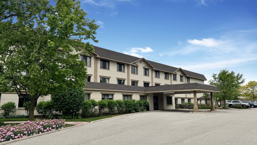 A three-story hotel building with an entrance and parking area surrounded by greenery.