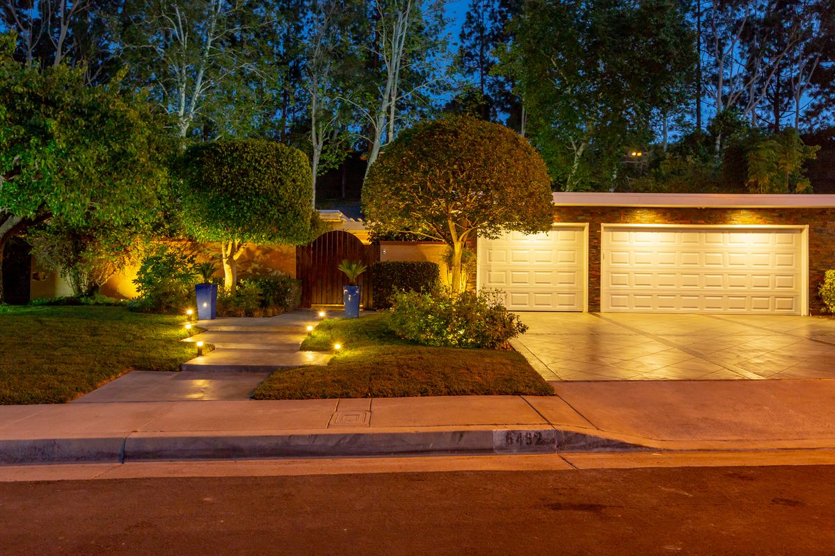 A well-lit house exterior and driveway with landscape lighting at night.
