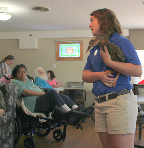 A presenter holds a bird of prey during an educational demonstration at a community center, engaging with residents and providing insights about the animal.