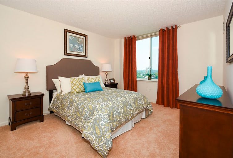 A well-decorated bedroom with a neatly made bed, warm-colored curtains, and a window view.