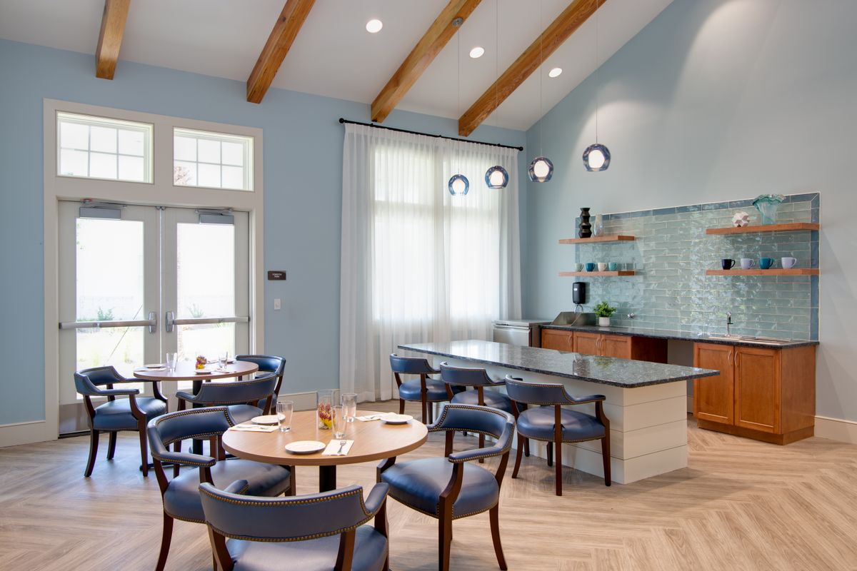 A modern dining area with wooden beams and a kitchen island, featuring blue walls and plenty of natural light.