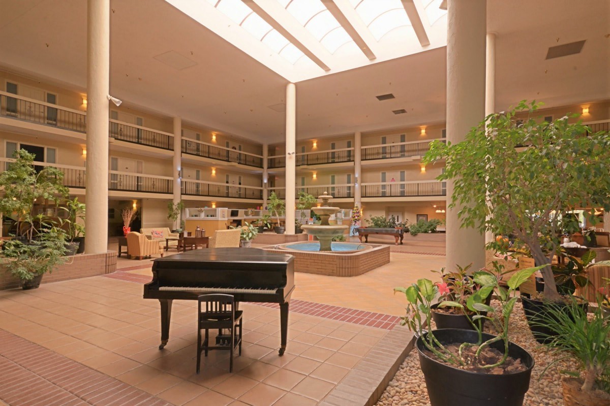 A spacious hotel atrium featuring a piano, fountain, and abundant natural light from the skylights.