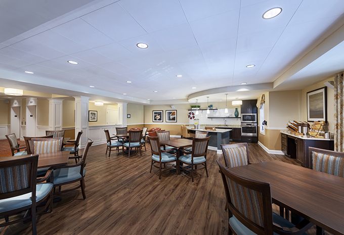 A spacious dining area with tables and chairs, featuring a kitchen in the background and wooden flooring.