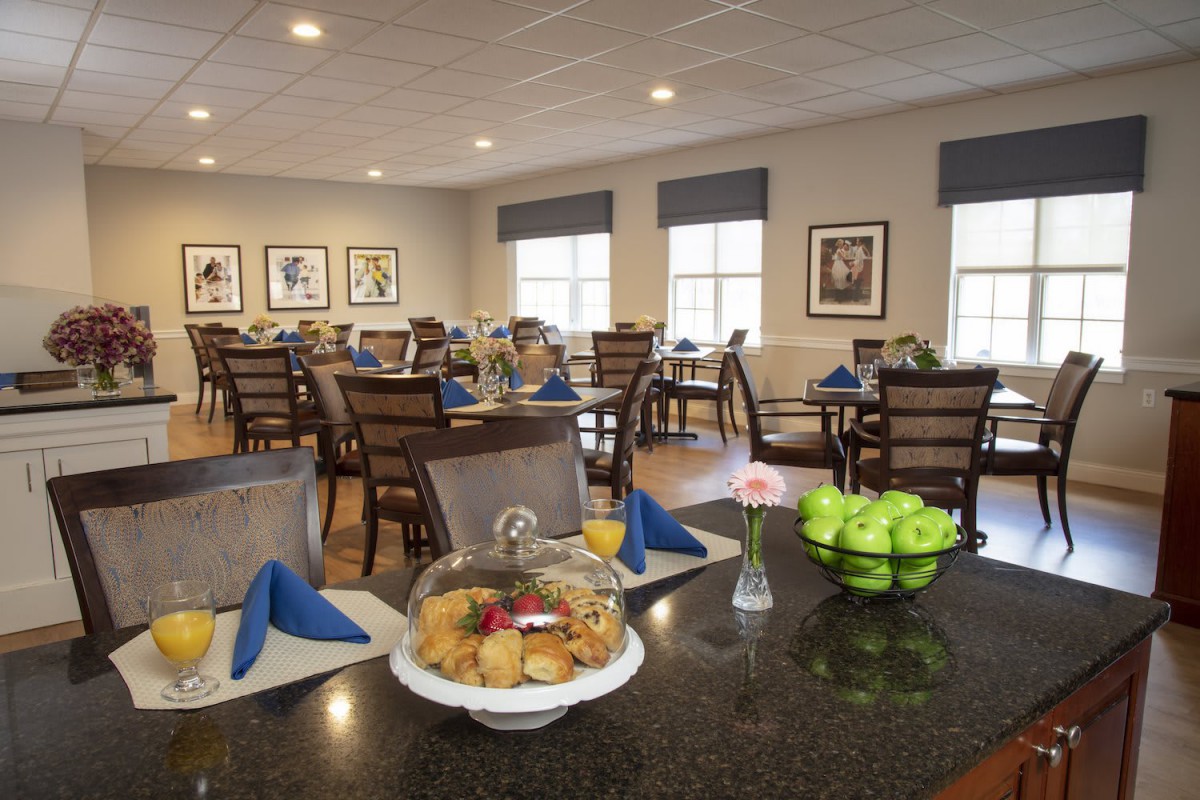 A well-lit dining room with neatly arranged tables and chairs, featuring a fruit platter centerpiece.