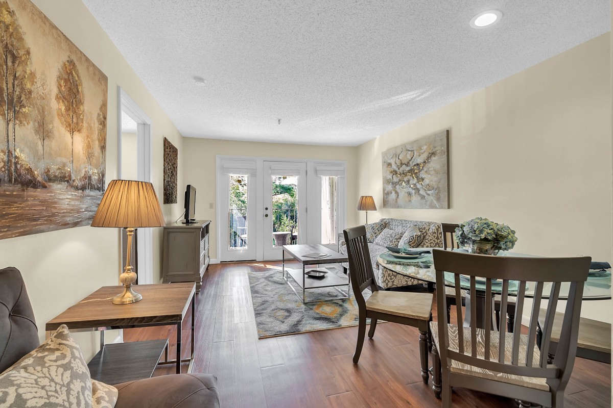 A cozy living room with wooden flooring, featuring a sofa, coffee table, and dining area.