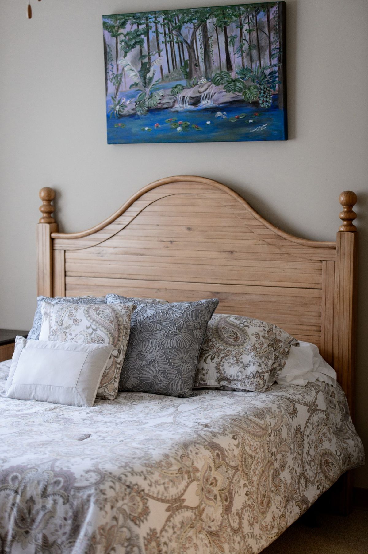 A cozy bedroom with a wooden headboard, decorative pillows, and a painting on the wall.