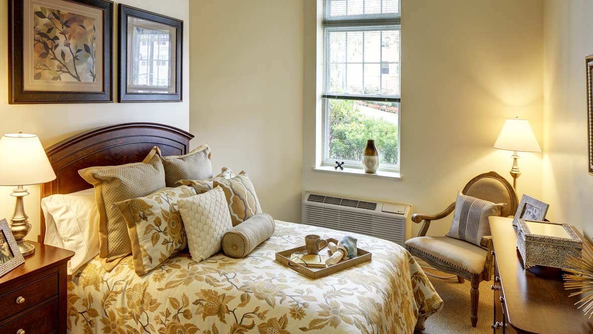 A cozy bedroom with a nicely decorated bed, featuring plush pillows and a tray. A window allows natural light to enter, complementing the warm interior design.