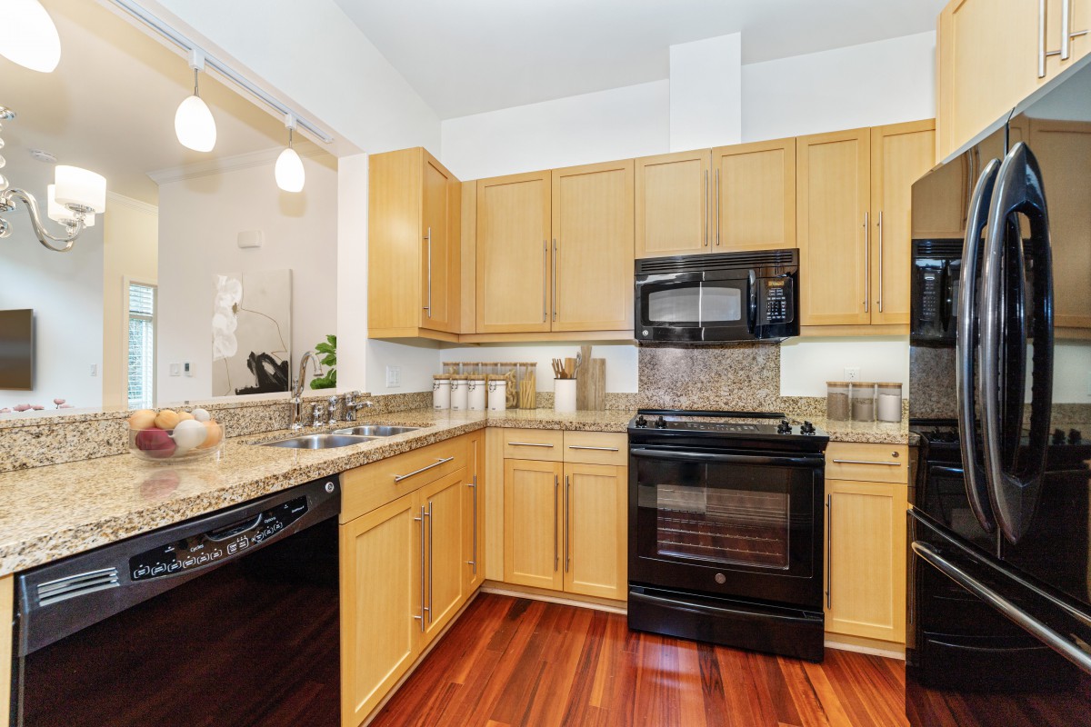 A modern kitchen with light wood cabinets, granite countertops, and black appliances.