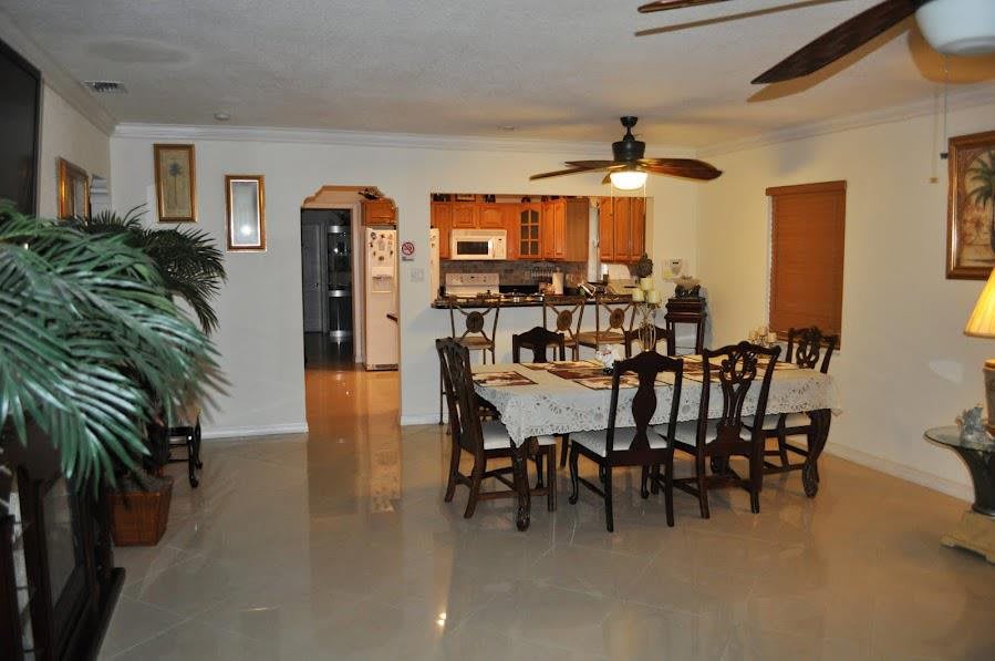 A spacious dining area connected to a kitchen, featuring a large dining table with multiple chairs and a ceiling fan overhead.