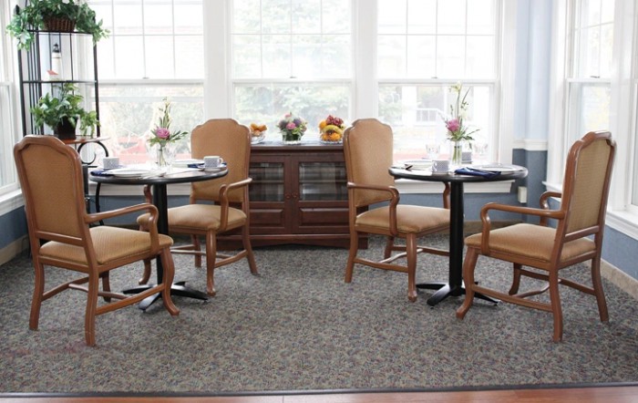 A cozy dining area with tables and chairs near large windows, adorned with flowers.