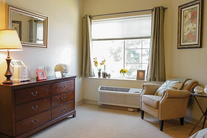 A cozy room with a large window, armchair, and dresser.