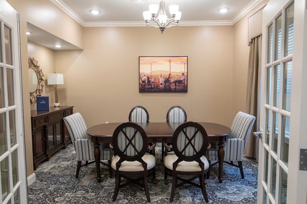 A well-lit dining room featuring a wooden table with six chairs, a chandelier, and artwork on the wall.