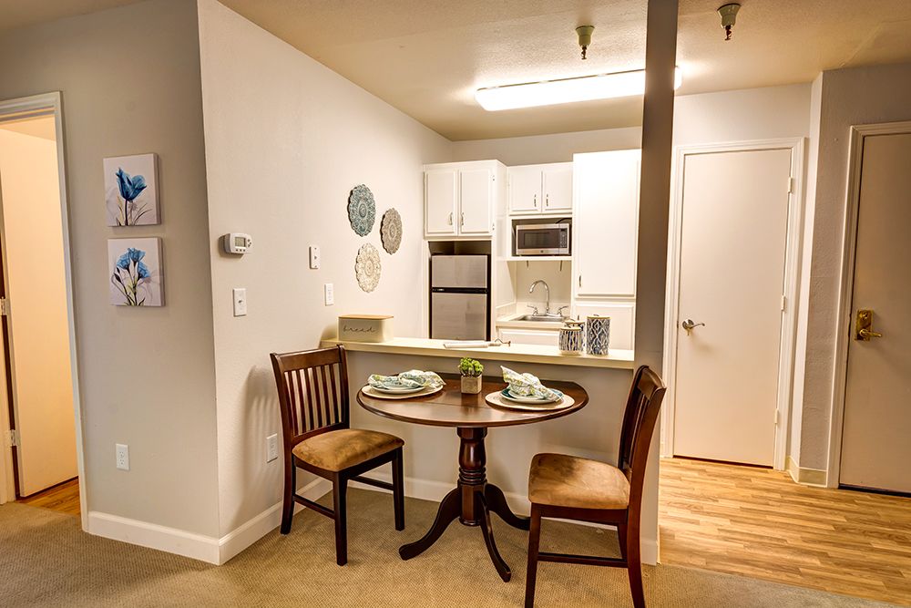 A cozy dining area with a small round table and two chairs, adjacent to a modern kitchen in an apartment.