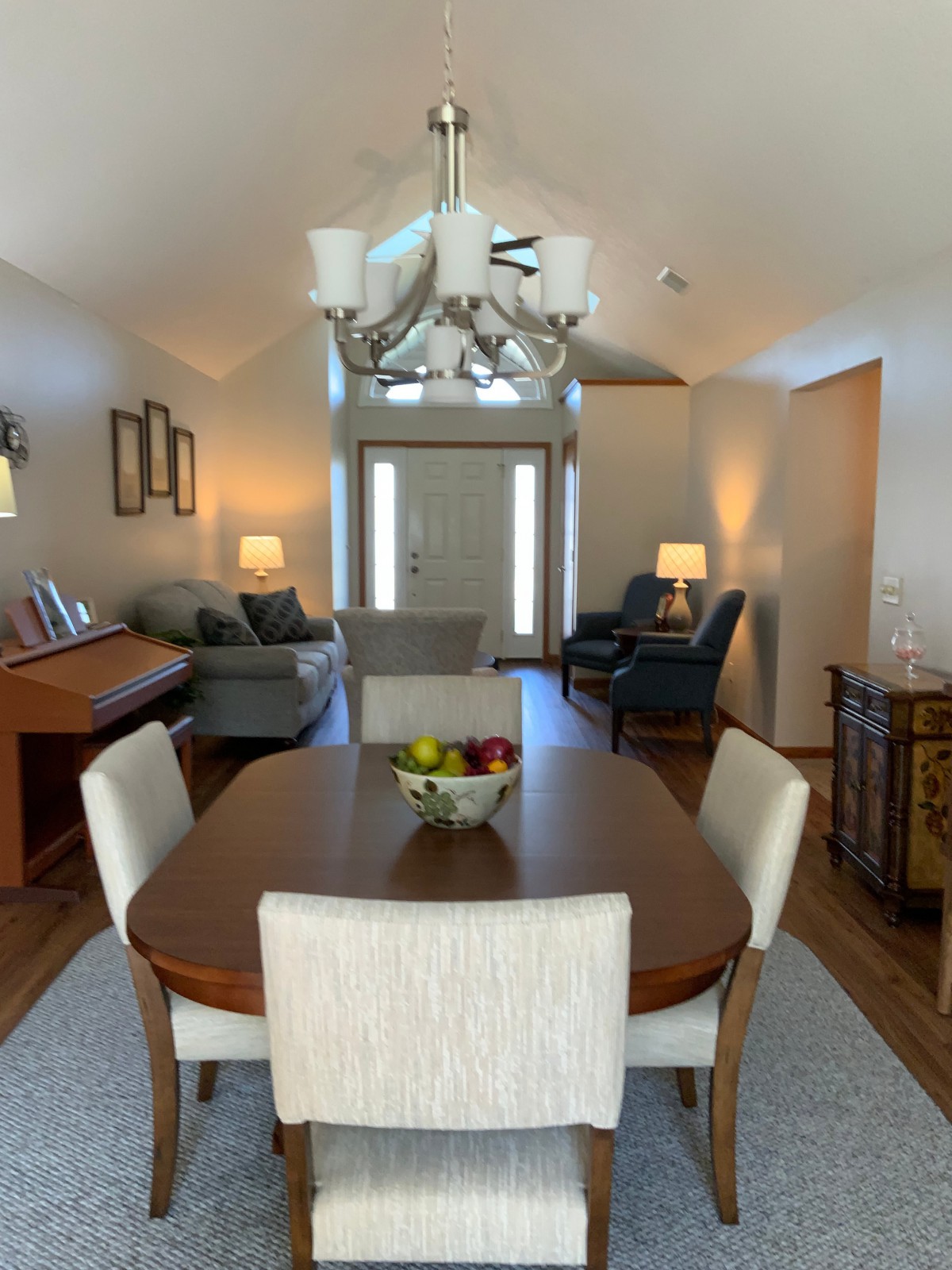 A cozy home interior featuring a dining table set, chandelier, and living area with sofas and a piano.