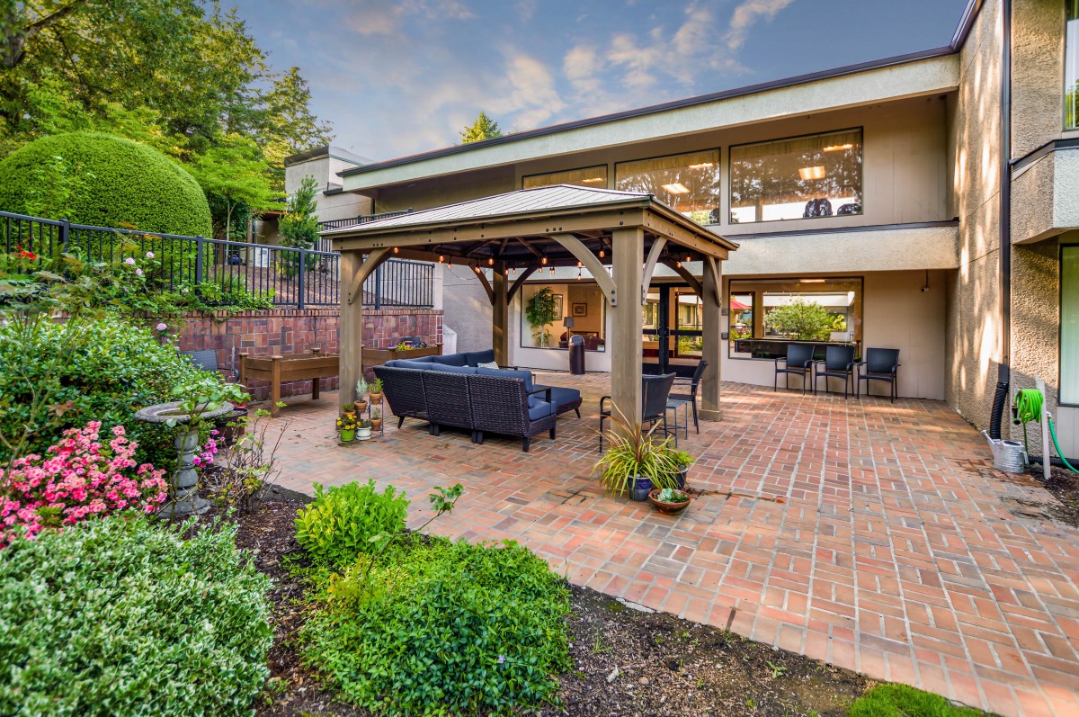A beautifully landscaped patio with a wooden pergola and outdoor furniture, set in a residential garden during the evening.