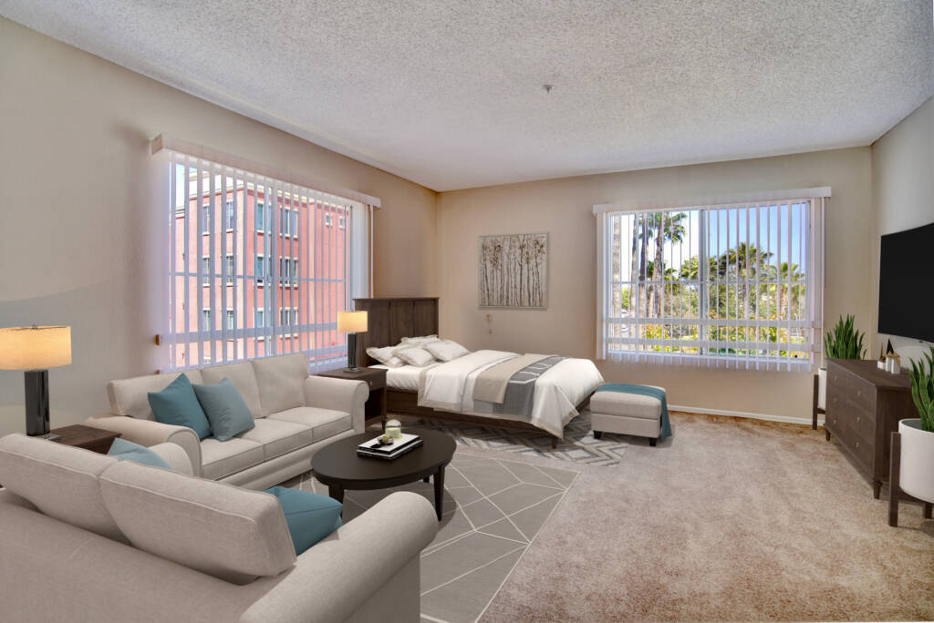 A spacious bedroom with a cozy seating area, featuring a bed and sofa near large windows that let in ample natural light.