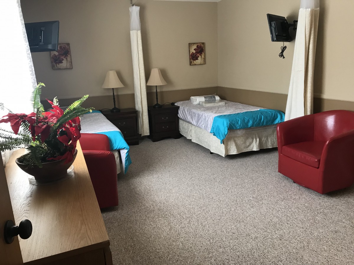 A hospital room with two beds, a curtain divider, and a television mounted on the wall.