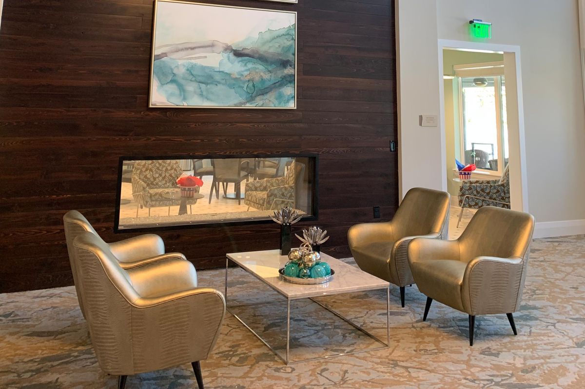 A modern lounge area featuring comfortable chairs, a central table, abstract artwork, and a sleek fireplace.
