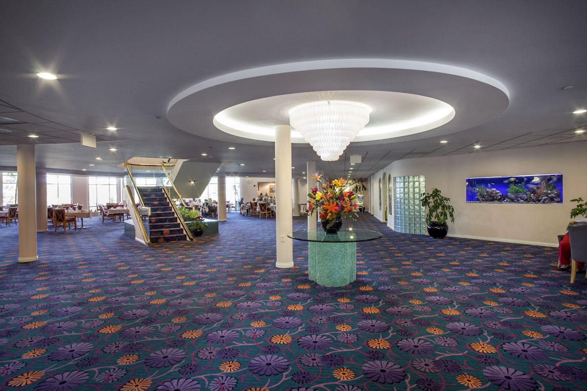 A spacious lobby area with a modern chandelier, vibrant carpet, and a central staircase.